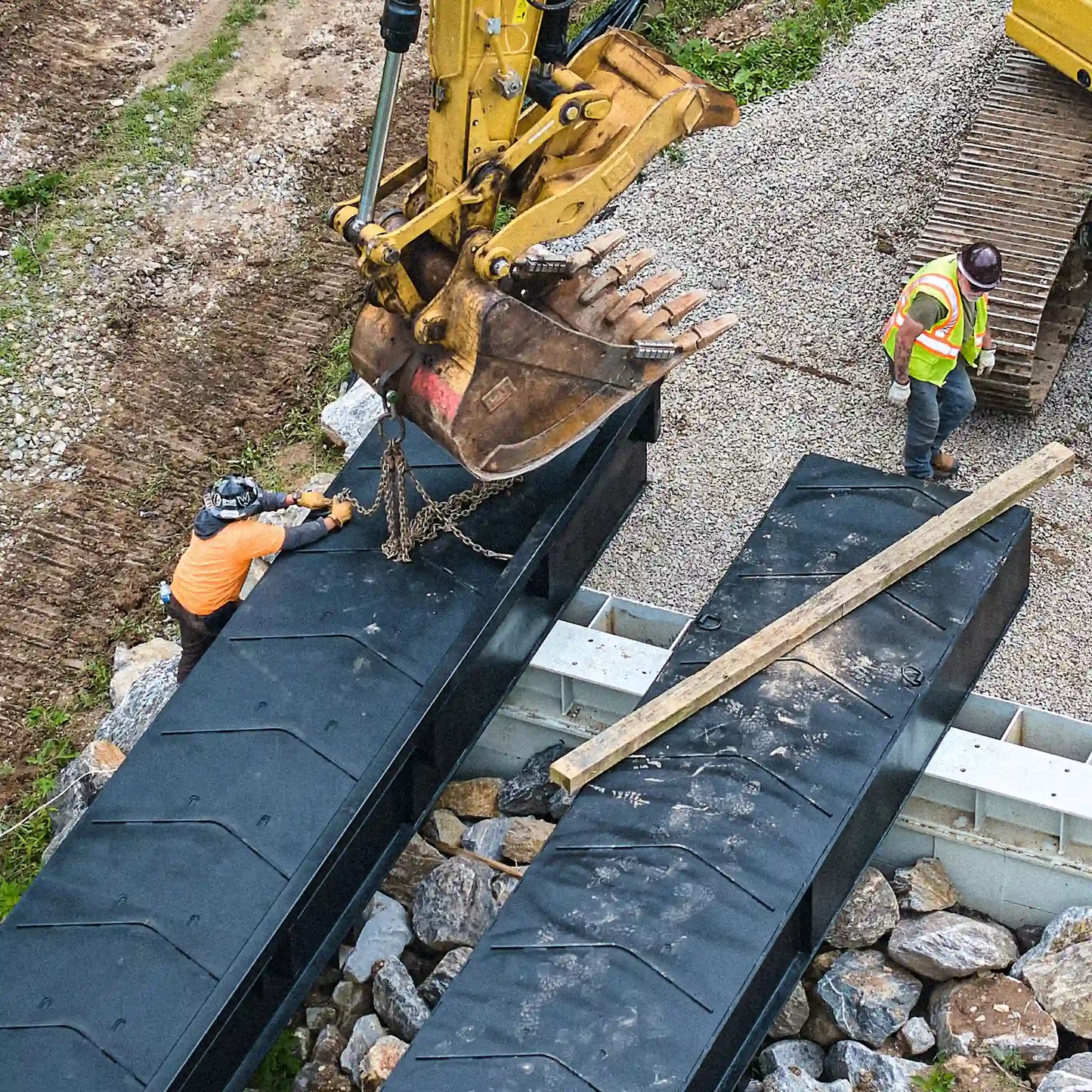 Crew setting a modular steel bridge over a creek with an excavator