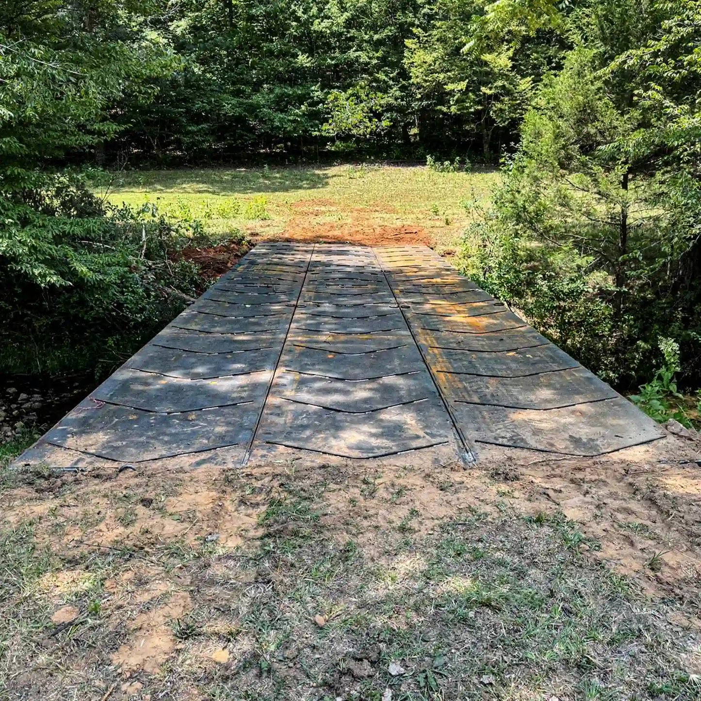 Steel construction bridge installed over a rocky creek with an excavator and pickup trucks on the far approach in a wooded work area.