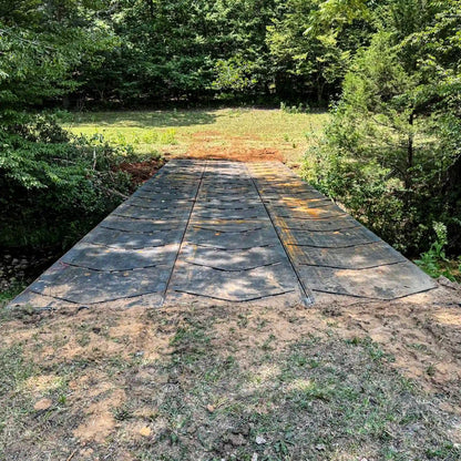Steel construction bridge installed over a rocky creek with an excavator and pickup trucks on the far approach in a wooded work area.