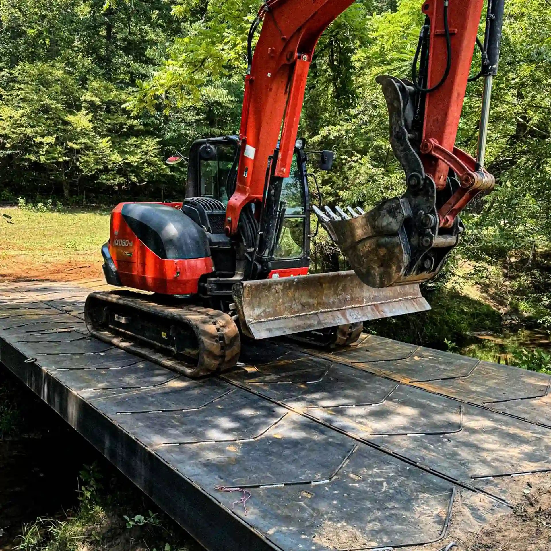 Front approach view of a modular steel construction bridge spanning a creek in winter, with workers gathered at the far end.