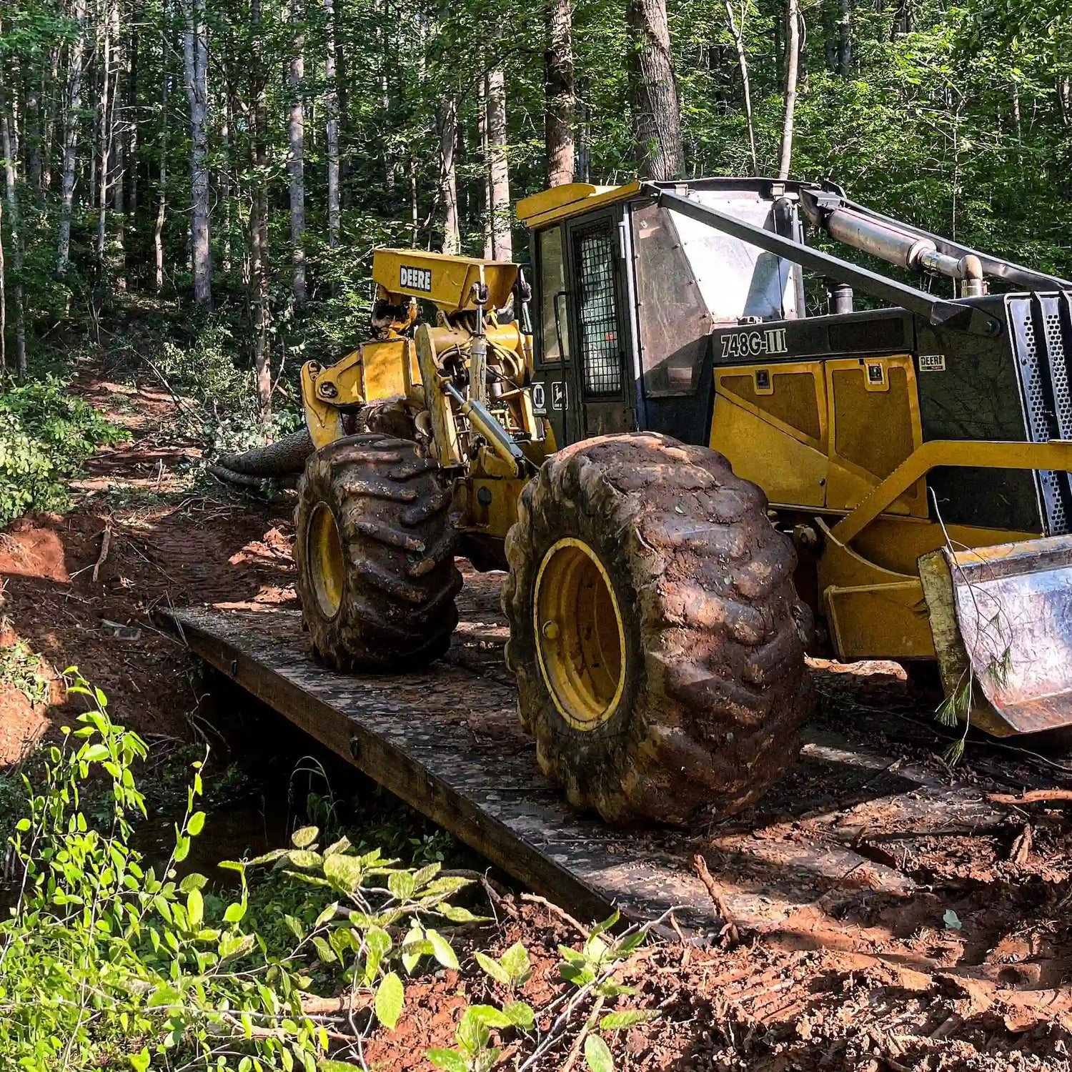 John Deere forestry skidder crossing a modular steel logging bridge in the woods during timber operations.
