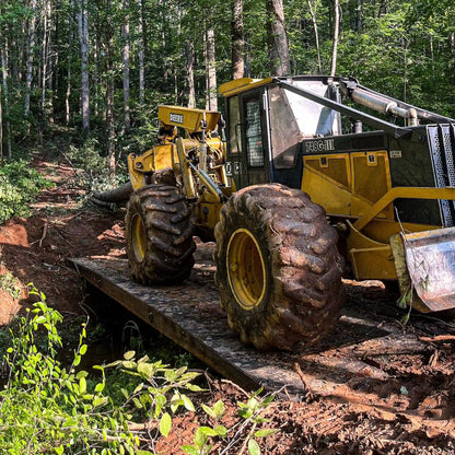 John Deere forestry skidder crossing a modular steel logging bridge in the woods during timber operations.