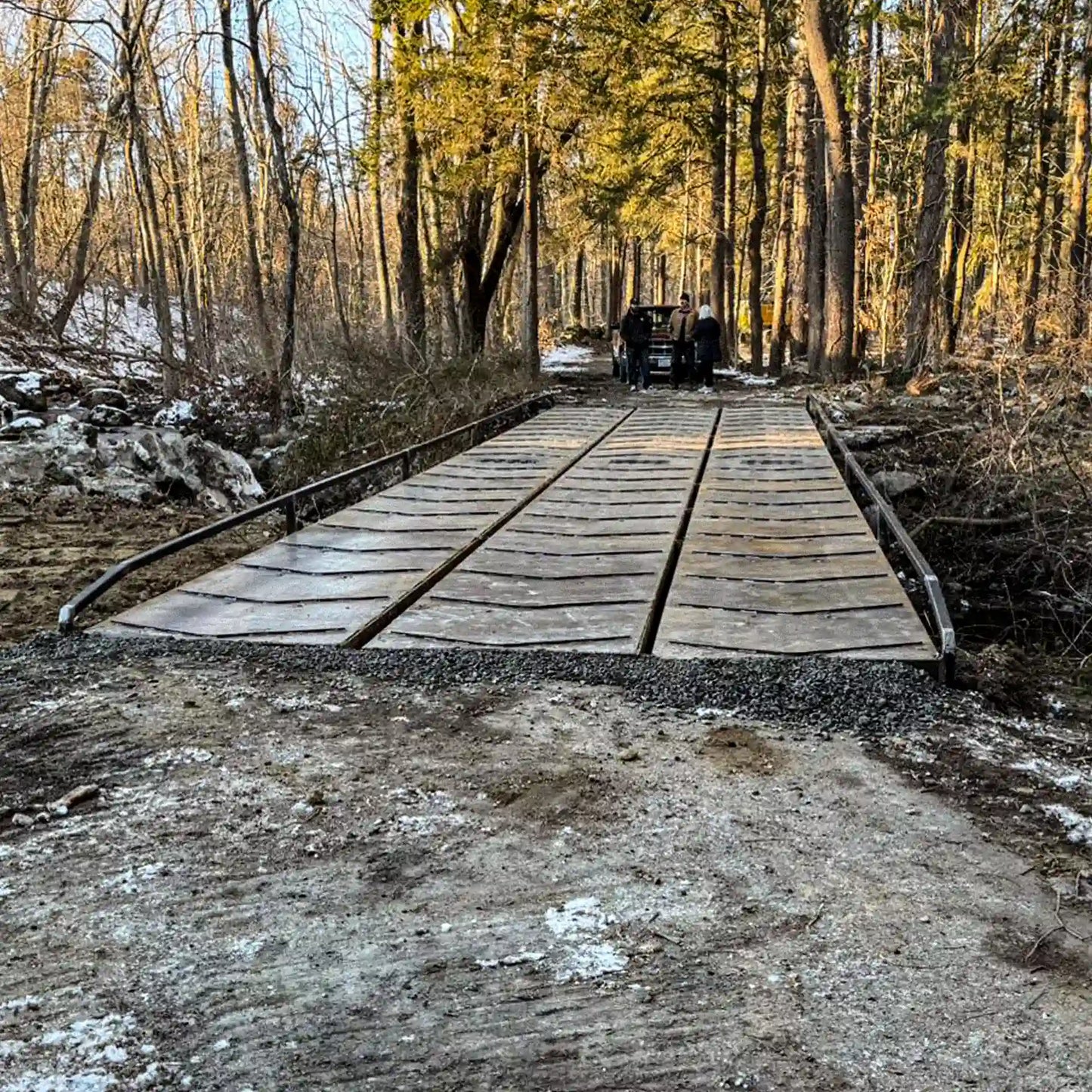 Front approach view of a modular steel logging bridge installed in a forest, showing the deck surface and side railings.