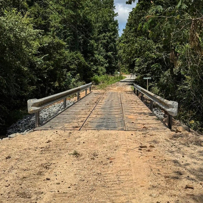 portable steel bridge with a railing over a stream in a wooded area