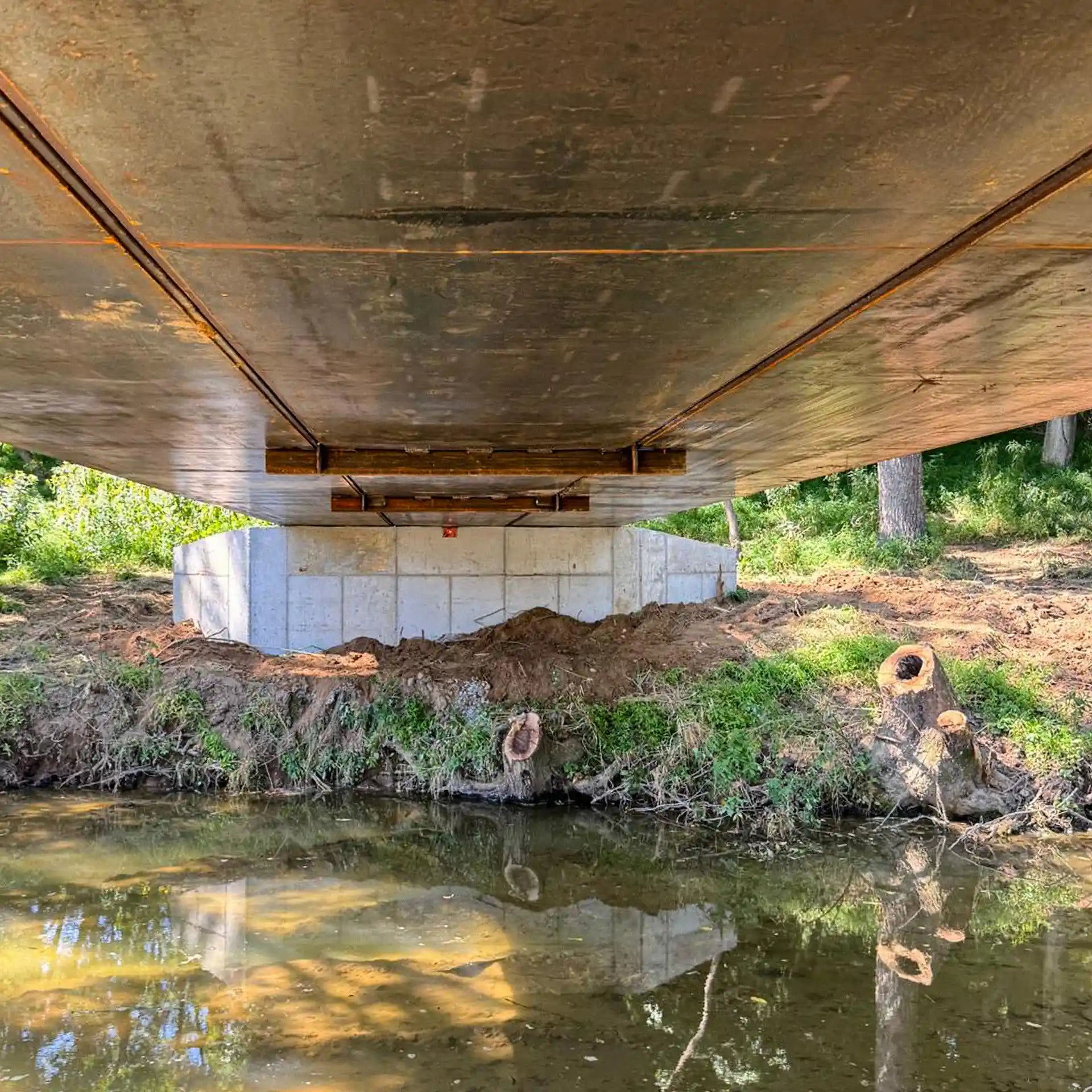 the underside of a portable steel bridge over a stream in a wooded area