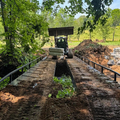 construction equipment on a portable steel bridge over a stream in a wooded area
