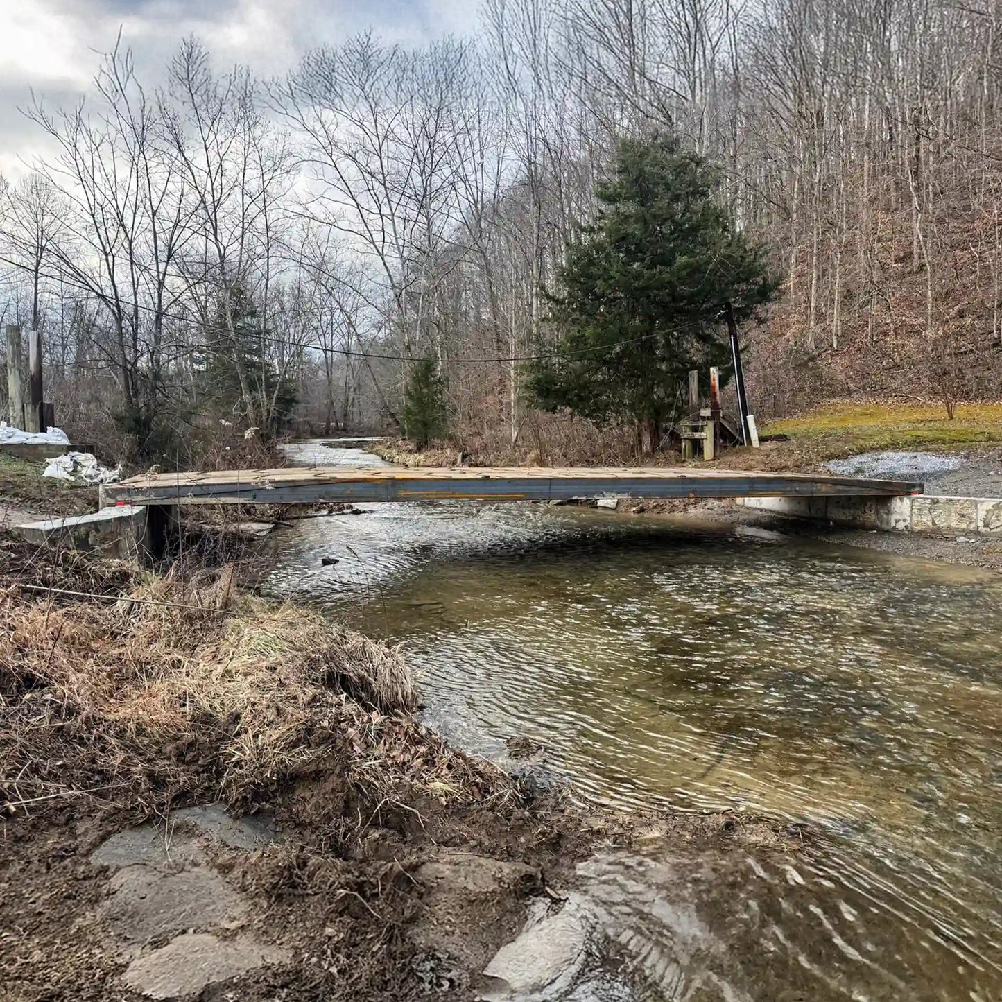 portable steel bridge over a stream in a wooded area with a cloudy sky in the background