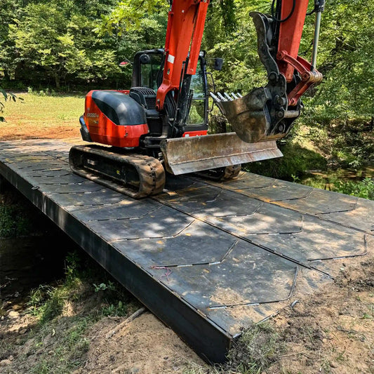 excavator on a portable steel bridge over a stream in a wooded area