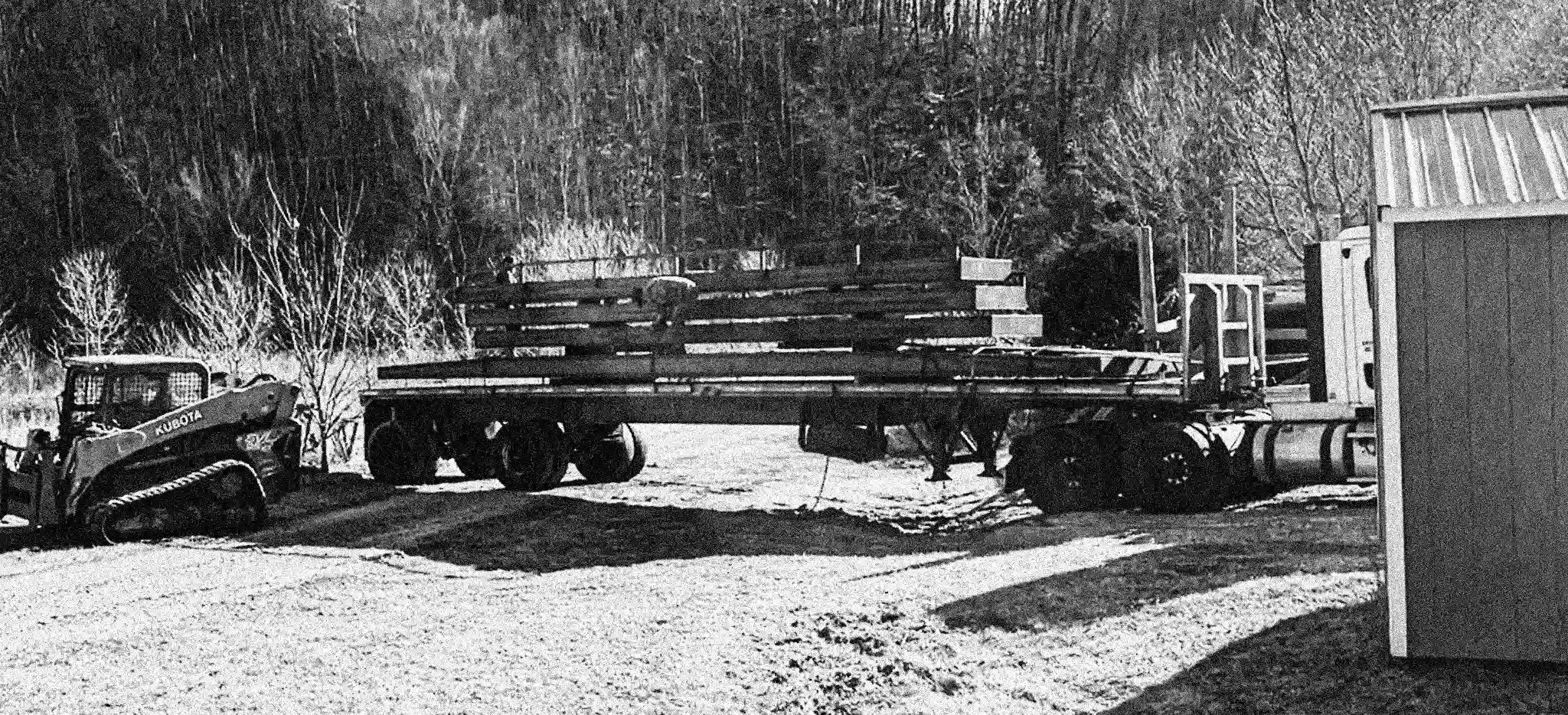 Truck with a flatbed carrying portable steel bridges in a wooded area