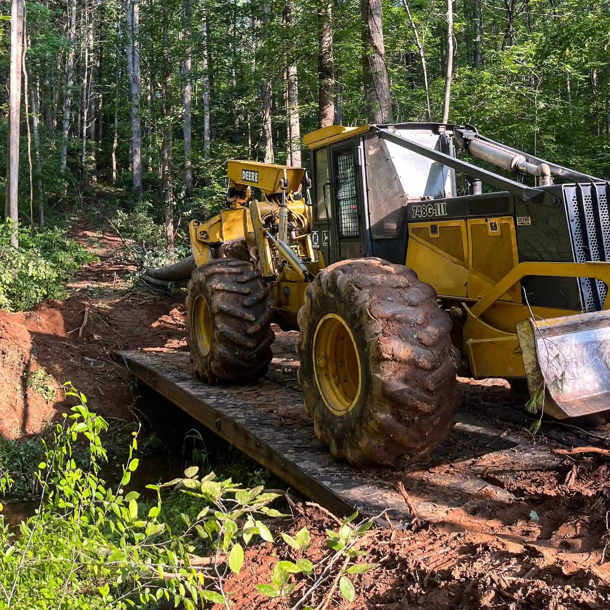 A logging machine on a portable steel bridge in a wooded area