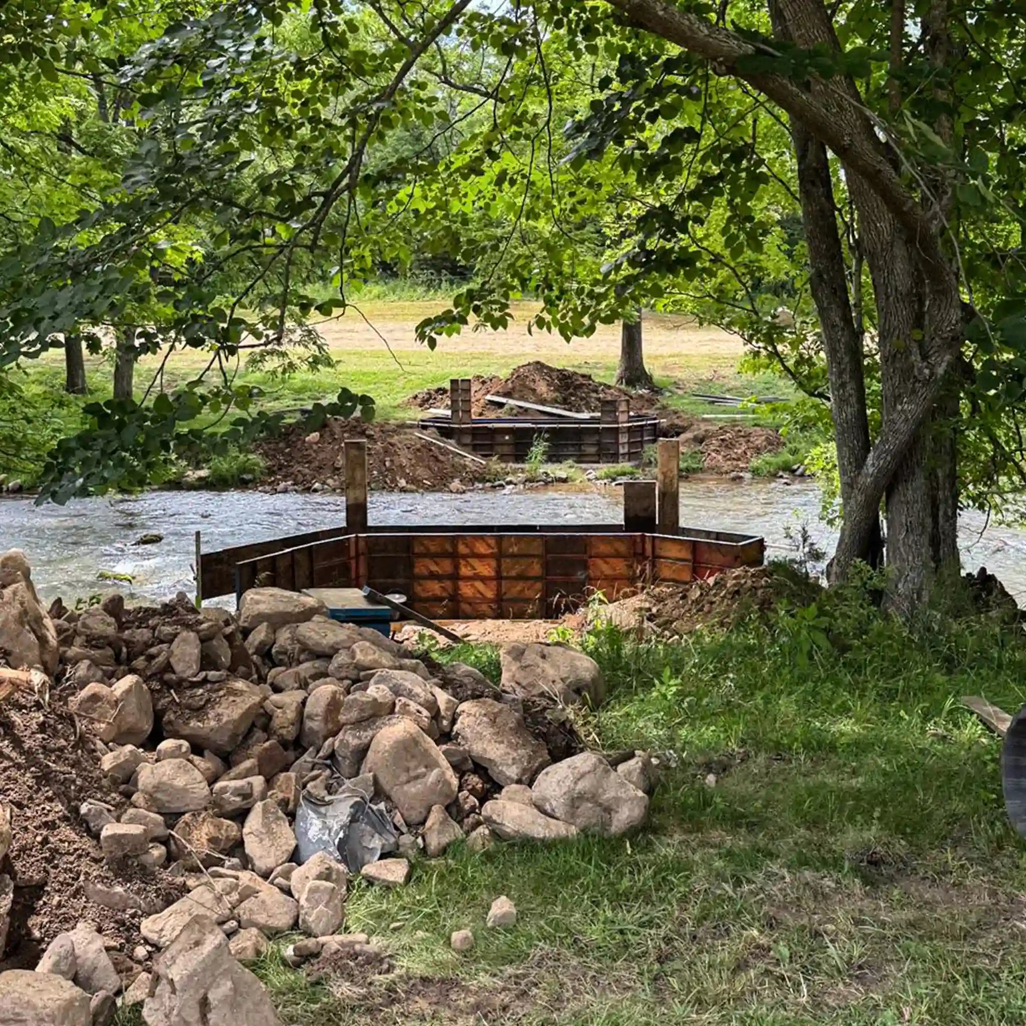 Construction site by a river with wooden frames and rocks.