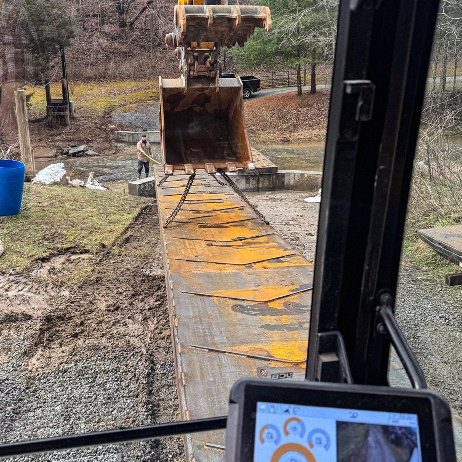 A portable steel bridge being installed over a stream in a wooded area