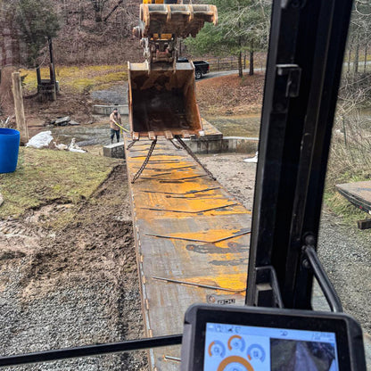 A portable steel bridge being installed over a stream in a wooded area