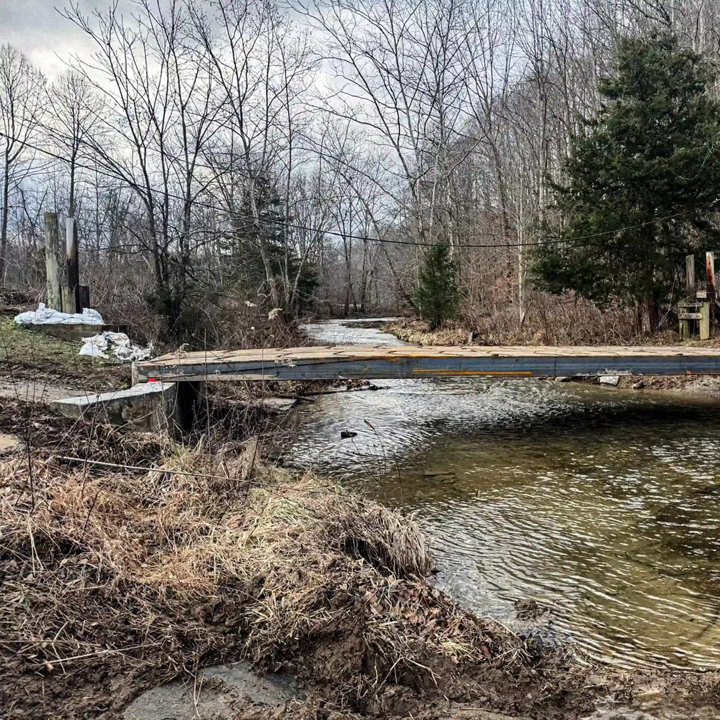 Side view of a modular steel residential bridge spanning a creek, connecting a rural driveway across a stream.