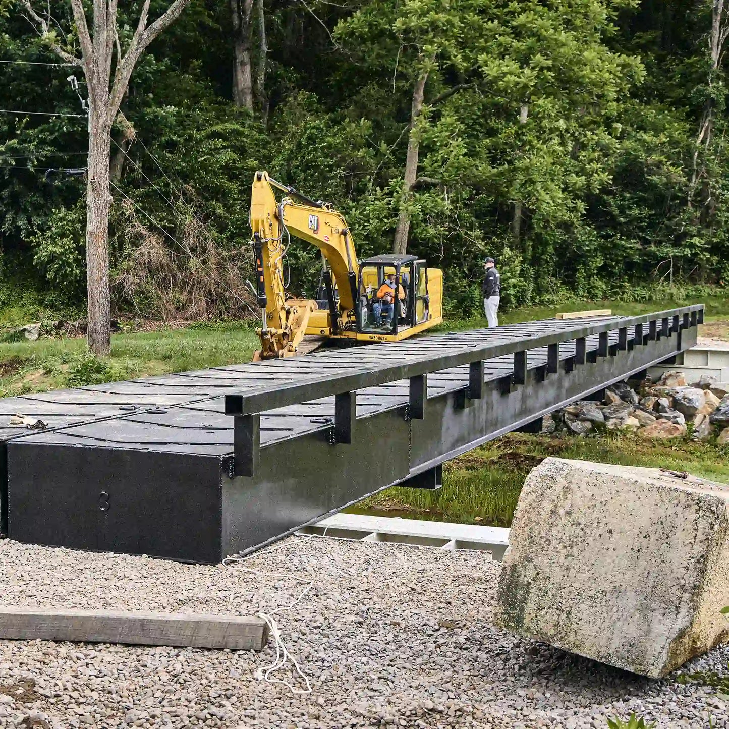 Black modular steel bridge installed across a rural creek crossing