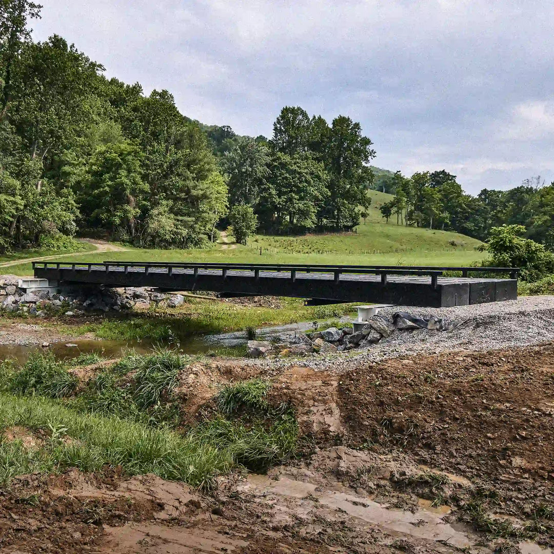 Black modular steel bridge crossing a creek in a rural valley