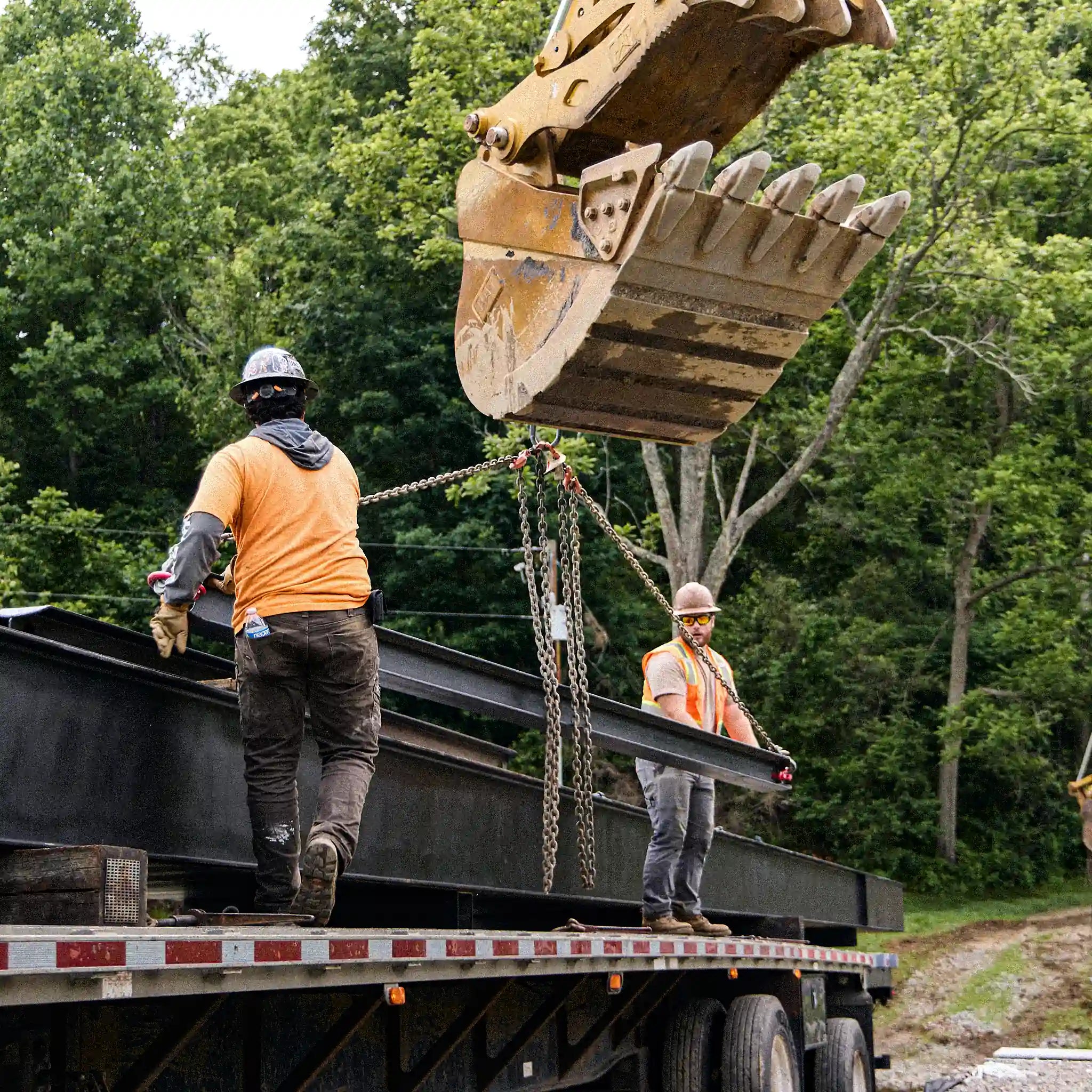 Crew loading a steel bridge beam onto a flatbed trailer