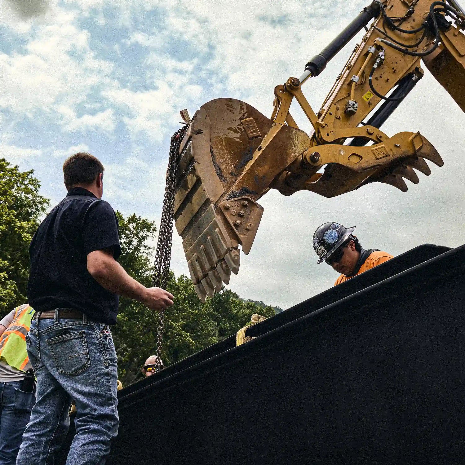 Crew rigging a steel bridge section with an excavator during installation