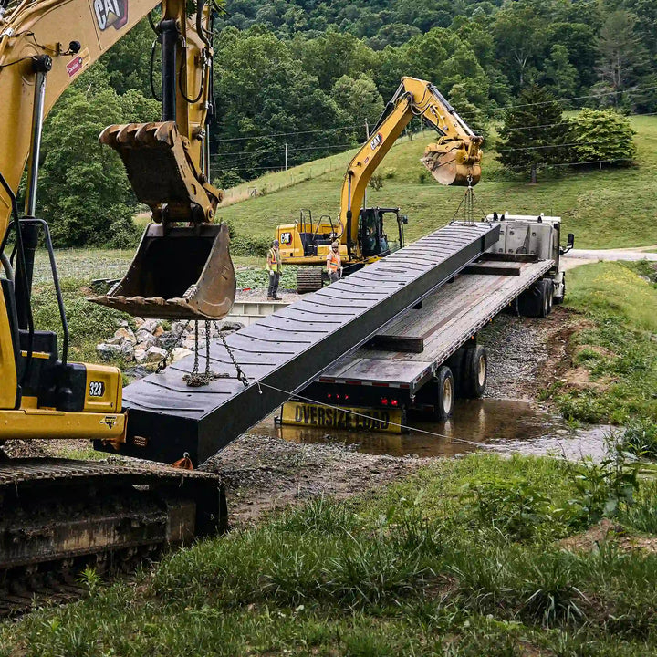 Excavators positioning a modular steel bridge section over a creek crossing