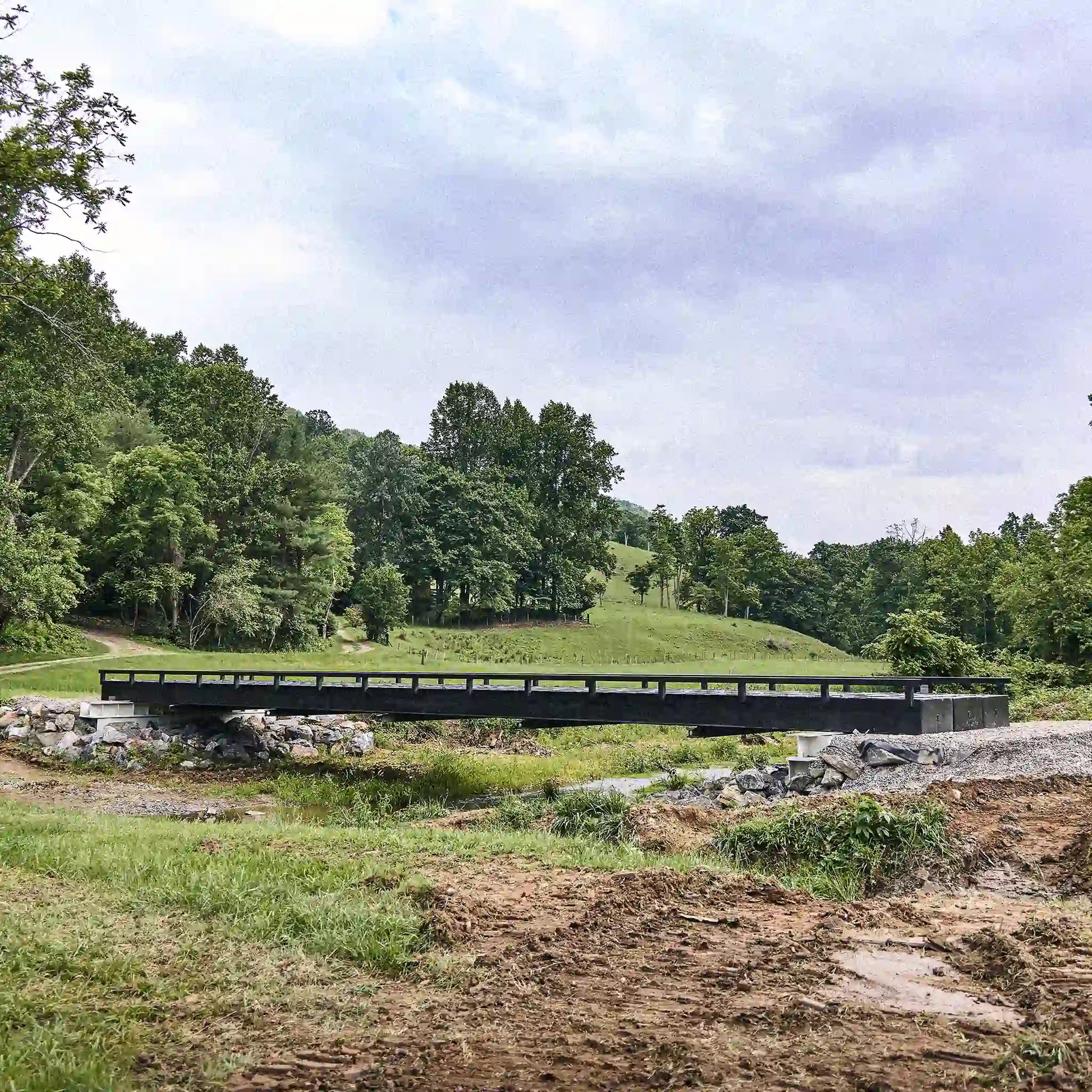 Black modular steel bridge crossing a creek in a rural valley