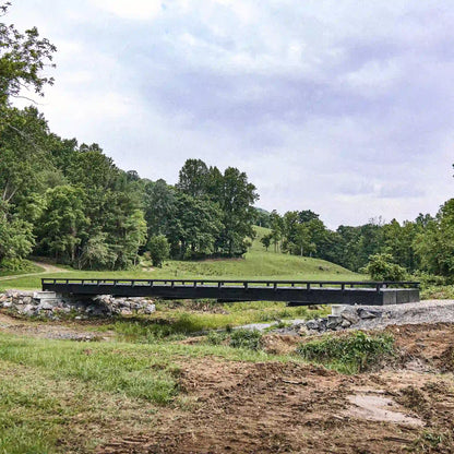 Black modular steel bridge crossing a creek in a rural valley
