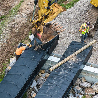 Crew setting a modular steel bridge over a creek with an excavator