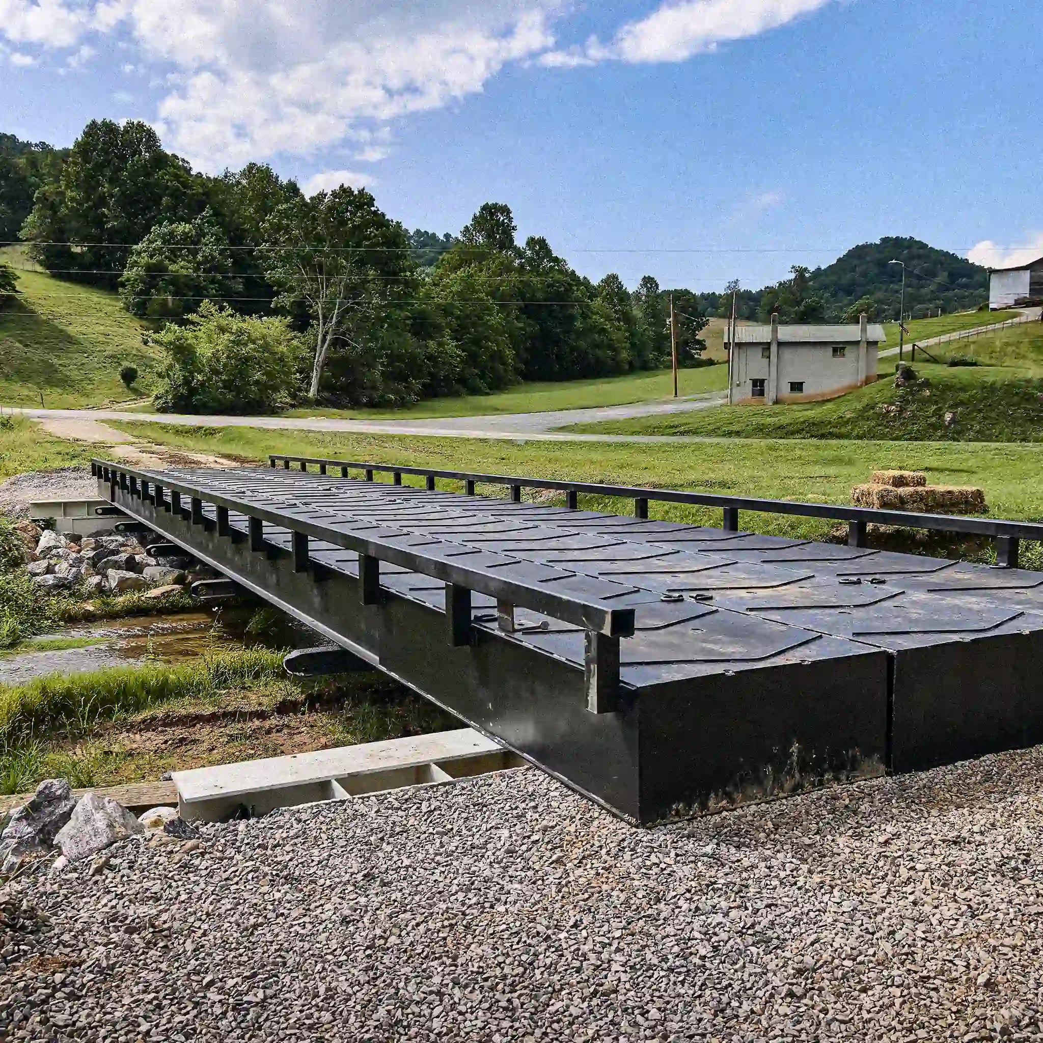 Modular steel bridge with guardrails installed over a rural stream