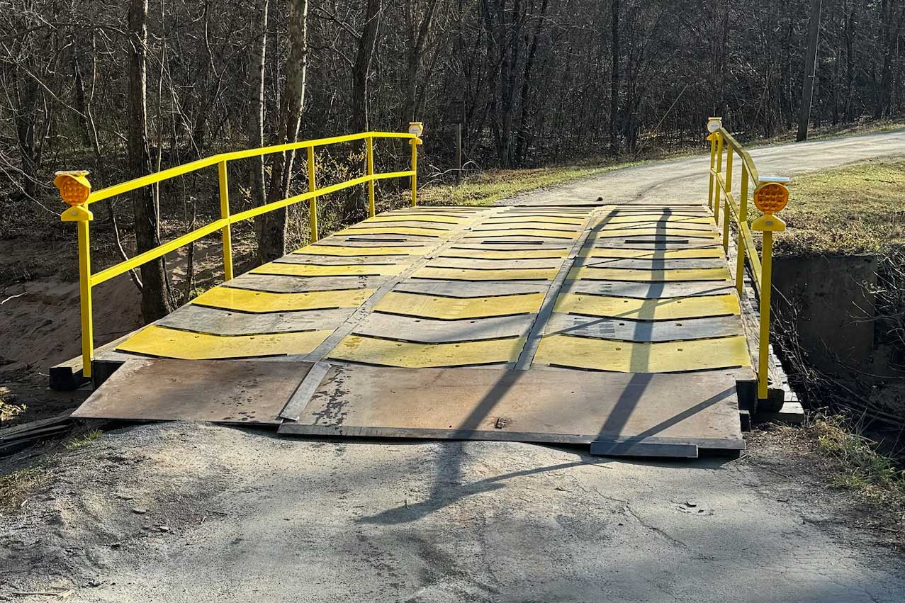 portable steel bridge with yellow pedestrian railings in a wooded area