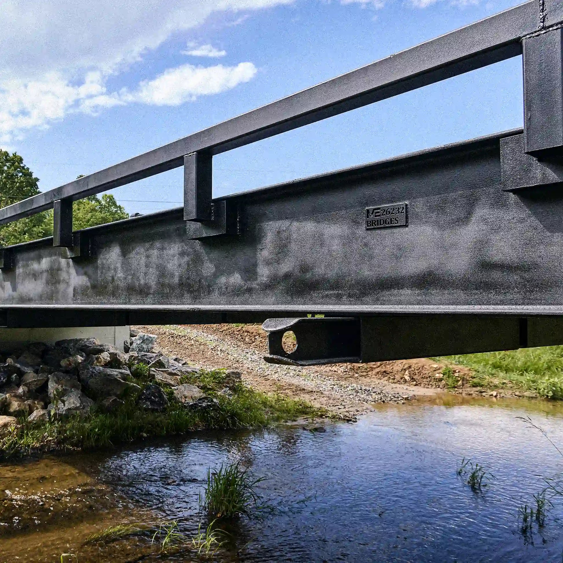 Close-up of steel bridge girder and rail system above a creek crossing