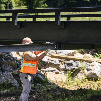 Worker guiding a steel bridge section into place above a creek crossing