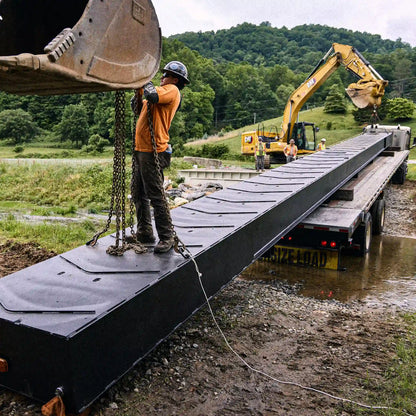 Worker rigging a modular bridge section on a flatbed trailer